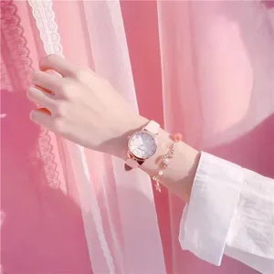 Close-up of a pink leather strap watch with a gold moon and star bracelet on a wrist