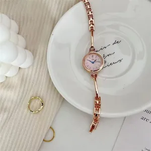 Detailansicht einer roségoldenen Damenuhr mit feinem Kettenarmband auf edlem weißem Porzellan