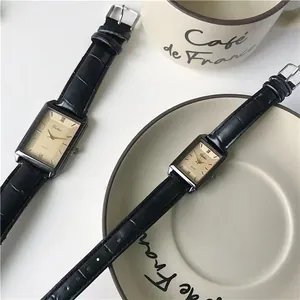 Macro detail of rectangular quartz watch with gold dial and black leather strap texture