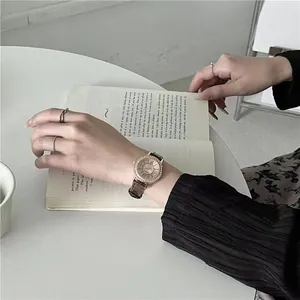 Detail of rose gold rhinestone watch with brown leather strap worn while reading
