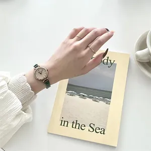 Primer plano de un reloj retro de cuarzo dorado con correa fina de cuero verde oscuro
