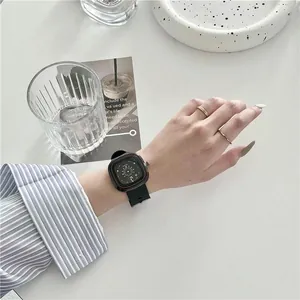 Detailopname van het vierkante zwarte horloge met rode randen en datum op de pols