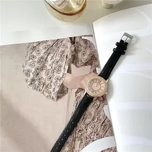 Close-up of rose gold crystal watch face with black crocodile leather strap on a magazine