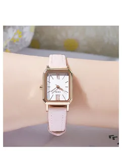 Gros plan d'une montre rectangulaire en or avec cadran blanc et bracelet en cuir rose