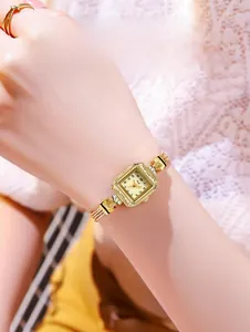 Détail d'une montre carrée dorée de luxe avec bracelet tressé en métal au poignet d'une femme
