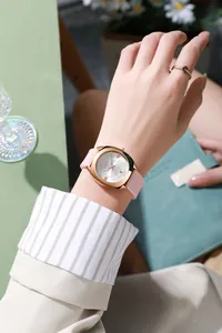 Detail van een roségouden tonneau-horloge met roze band en datumweergave om de pols