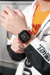 Detail of square quartz watch with black dial, gold markers, and red silicone strap