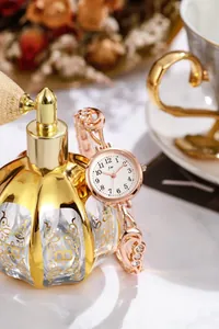 Dettaglio dell'orologio al quarzo in oro rosa con strass accanto a un profumo vintage