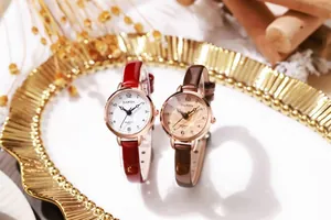 Close-up of minimalist quartz watches with slim red and brown straps in a gold tray