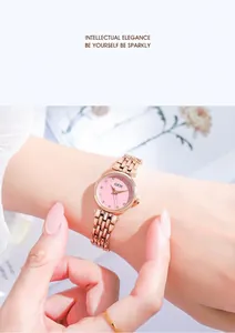 Detail of rose gold watch with pink dial and diamond markers on a light blue background
