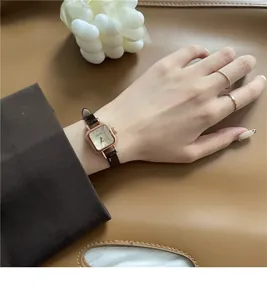 Dettaglio orologio vintage quadrato con cinturino in pelle marrone indossato al polso