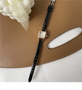 Dettaglio dell'orologio quadrato oro rosa con cinturino in pelle verniciata nera su base