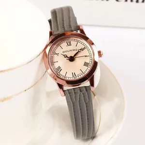 Gros plan d'une montre vintage en or rose avec bracelet en cuir gris sur une tasse blanche