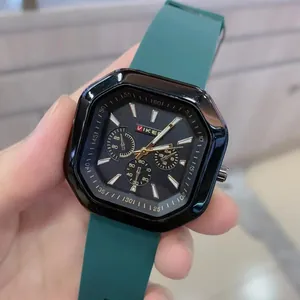 Close-up of a square black quartz watch with green silicone strap and chronograph details