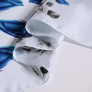 Detailed view of silk-like white scarf featuring vibrant blue floral patterns and satin gloss