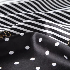 Detail view of silk-like scarf featuring black and white stripes and polka dot patterns