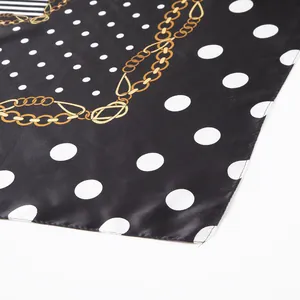 Detailed view of black silk scarf featuring white polka dots and golden chain patterns