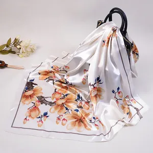 Foulard carré en satin de soie avec imprimés magnolia jaune posé sur un sac