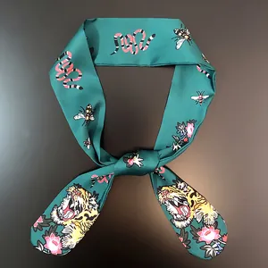 Close-up of dark green satin scarf featuring vibrant snake, bee and floral patterns