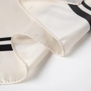 Macro shot of ivory silk scarf showing premium satin texture and black stripe detail