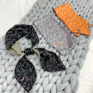 Three long silk scarves with bird patterns in black, grey, and orange on a knit background