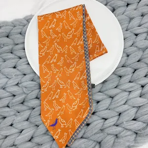 Close-up of orange bird print twilly silk scarf on a white plate with knit background