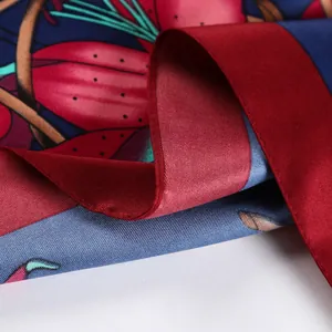 Detailed close-up of dark blue silk scarf featuring red floral patterns and rolled edges