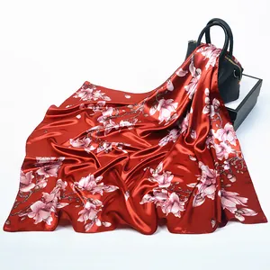 Dettaglio di un foulard di seta rossa con fiori di magnolia drappeggiato su una borsa nera