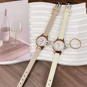 Detail of two women's quartz watches with slim beige and cream leather straps on a tray