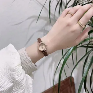 Close-up of small round gold dial watch with slim brown leather strap on a wrist