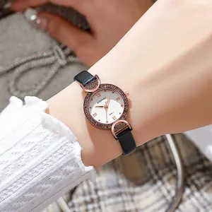 Nahaufnahme einer Damenuhr in Roségold mit Strass-Lünette und schwarzem Lederarmband