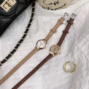 Detail of small rose gold quartz watches with slim brown leather bands on white fabric