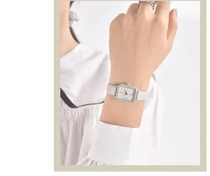 Gros plan de la montre carrée pour femme avec cadran blanc et bracelet en cuir gris