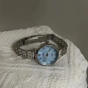 Détail montre BARSH en métal argenté avec cadran bleu clair sur tricot blanc élégant