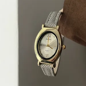 Gros plan d'une élégante montre ovale dorée avec cadran champagne et bracelet en cuir gris