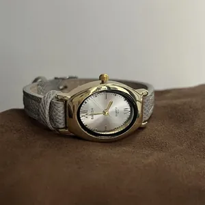 Vue macro d'une élégante montre ovale dorée avec bracelet en cuir gris sur daim marron