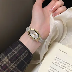 Detailopname van elegant goud ovaal horloge met kristallen ring en grijze leren band