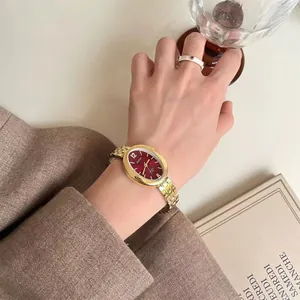 Dettaglio macro dell'orologio ovale dorato con quadrante bordeaux e cinturino in metallo