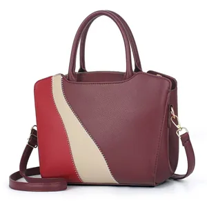 Detail van bordeauxrode handtas met kleurblokken, witte stiksels en gouden hardware