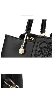 Close-up of black leather handbag featuring reinforced handles and pearl charm detail
