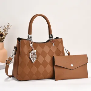Close-up of brown textured leather tote and matching clutch set with leaf charm detail