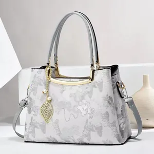 Close-up of elegant embroidery textures and gold leaf pendant on a white floral handbag