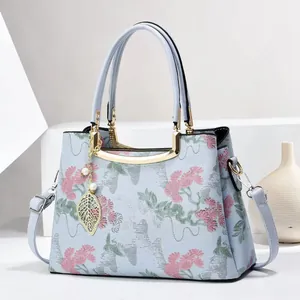 Light blue embroidered tote bag with pink floral patterns and golden metal handles