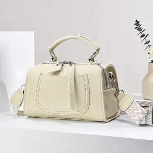 Detail of cream leather shoulder bag with logo, top handle and patterned jacquard strap