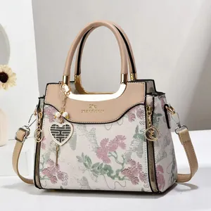 Detail of floral embroidery on beige handbag with gold hardware and heart charm