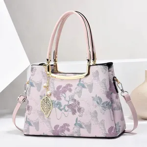 Elegant pink handbag with floral embroidery and gold leaf pendant in a minimalist setting