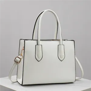 White Saffiano leather tote bag with gold hardware and adjustable strap on marble stand