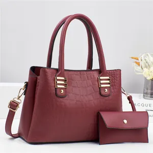 Detail of burgundy lychee and crocodile grain leather handbag set with golden hardware