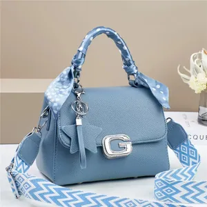 Detail of light blue crossbody bag featuring a silk scarf handle and wide woven strap