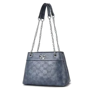 Blue crossbody bag with bow pattern texture and silver chain strap on white background